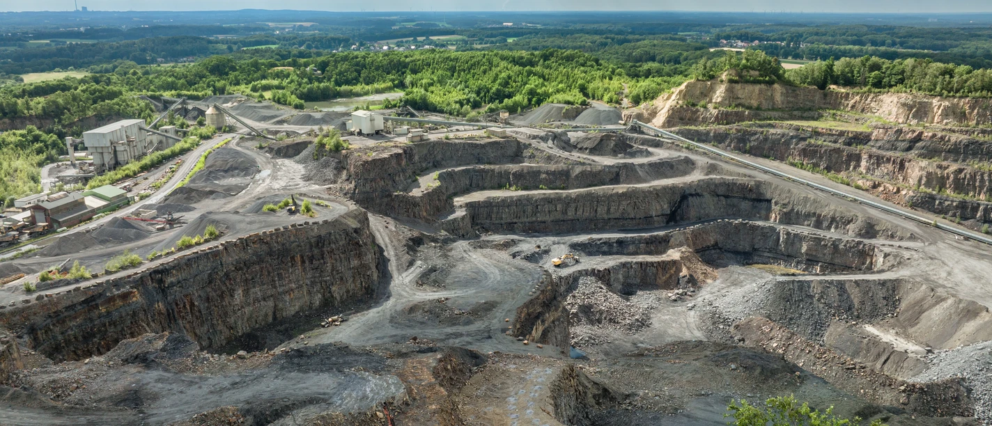osnabrueck-piesberg©tol-foto-max-wiesenbach (2).jpg Weitläufiger Steinbruch mit abgestuften Abbauflächen unter wolkenbedecktem Himmel.