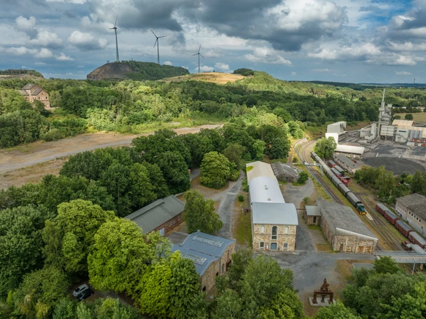 Museum Industriekultur Osnabrück Ehemaliges Industriegelände mit Zügen und Windturbinen in grüner Hügellandschaft.