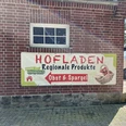 Hofladen Evers-Königschulte, Freren ©Emsland Tourismus GmbH (4).JPEG Werbeschild aus Stoff an roter Backsteinwand mit Aufschrift Hofladen Regionale Produkte Obst und Spargel
