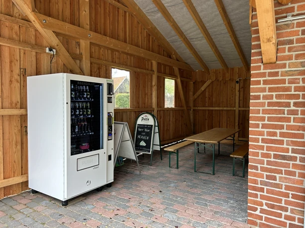 Hofladen Pott-Stopp Lingen Wachendorf ©Emsland Tourismus GmbH (4).JPEG Holzüberdachter Sitzbereich mit Verkaufsautomat für regionale Produkte und rustikaler Sitzgarnitur.