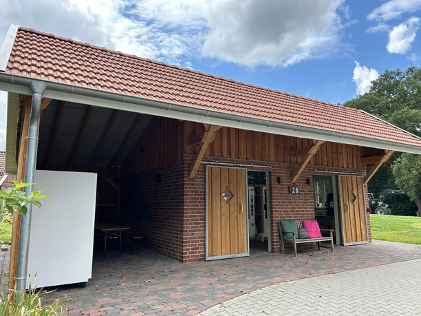 Hofladen Pott-Stopp Lingen Wachendorf ©Emsland Tourismus GmbH (9).JPEG Backsteinbau mit rotem Dach und Holzläden, davor Sitzbank und gepflasterter Weg unter blauem Himmel.