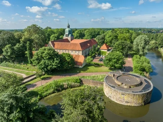 fuerstenau-schloss-copyright-tol-foto-max-wiesenbach.jpg Historisches Schloss inmitten üppiger grüner Landschaft mit Wassergraben und Rundturm im Vordergrund.