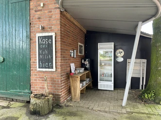 Käsehof Hüsing Freren Suttrup Verkaufsecke mit Kühlschrank und Holzregal für Käseprodukte an einer rotverblendeten Hofmauer.