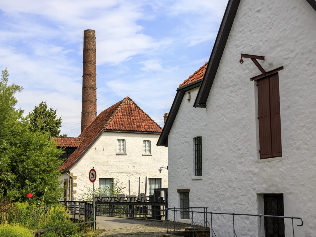 bramsche-tuchmacher-museum(c)tol-foto-jurjen-drenth (1).JPG Historische Backsteingebäude mit rotem Ziegeldach und Schornstein vor blauem Himmel.