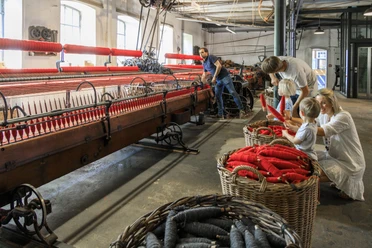 bramsche-tuchmacher-museum(c)tol-foto-jurjen-drenth (11).JPG Historic weaving mill with visitors, red yarn spools, old machines in a light-flooded room.