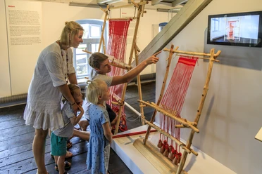 bramsche-tuchmacher-museum(c)tol-foto-jurjen-drenth (17).JPG Eine Familie betrachtet traditionelle Webrahmen in einem Museum.