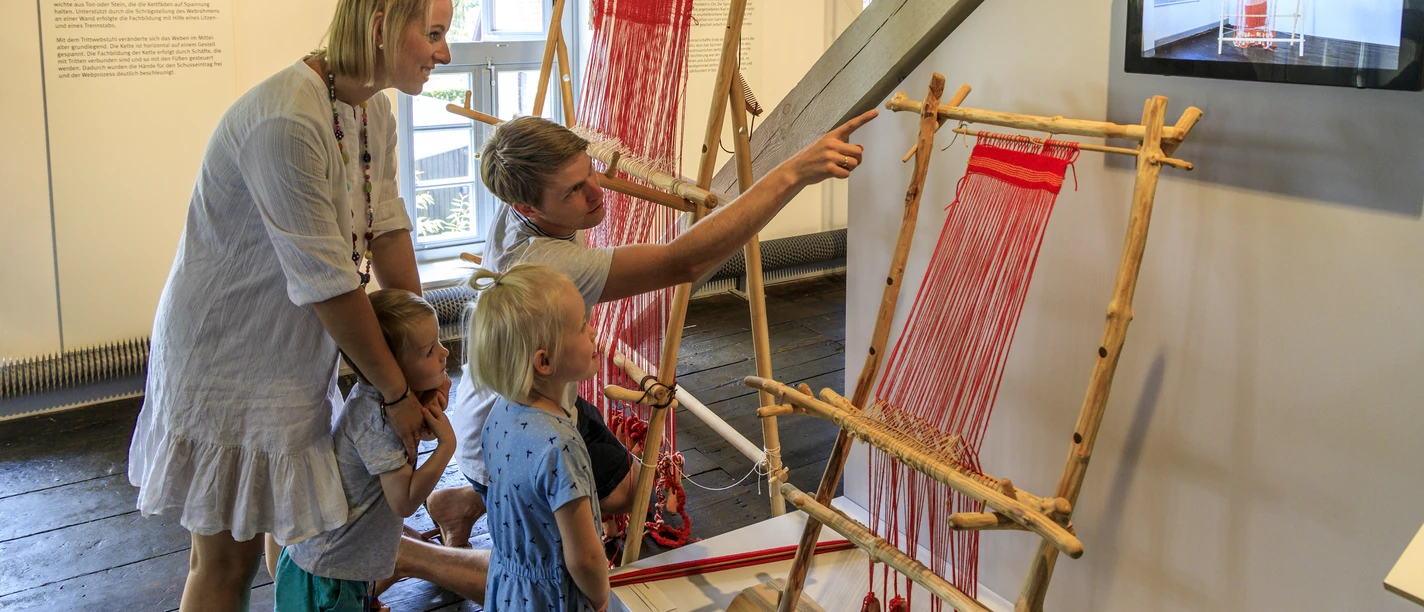 bramsche-tuchmacher-museum(c)tol-foto-jurjen-drenth (17).JPG Eine Familie betrachtet traditionelle Webrahmen in einem Museum.