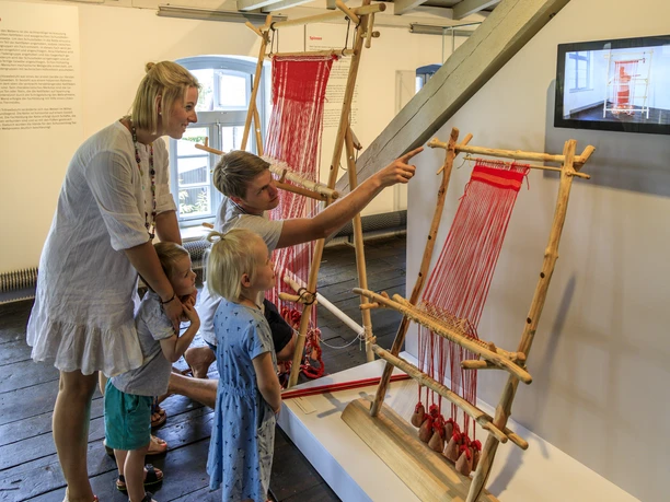 bramsche-tuchmacher-museum(c)tol-foto-jurjen-drenth (17).JPG Eine Familie betrachtet traditionelle Webrahmen in einem Museum.