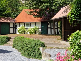 Fachwerkgebäude im Grünen mit roten Dächern, eingebettet in eine idyllische Gartenlandschaft.