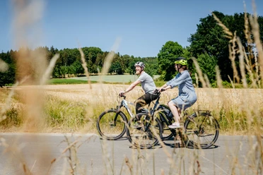 Radfahren im Osnabrücker Land Zwei Radfahrer mit Helmen fahren durch eine sonnige Landschaft mit Wiesen und Wald.