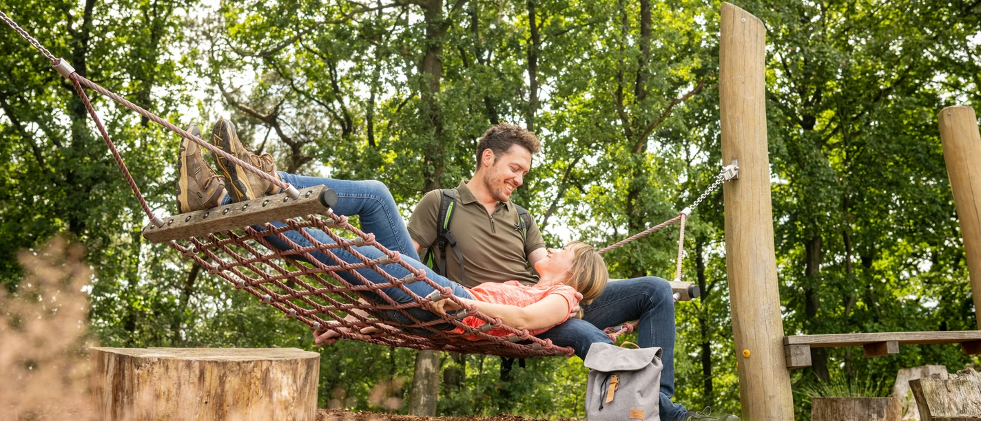Werther-Hermannshöhen-Teutoburger-Wald-Tourismus-D-Ketz-086.jpg Ein Paar entspannt in einer Waldaussicht auf einem Netzschaukelplatz, umgeben von grünen Bäumen.