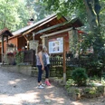 Ibbenbüren-Almhütte-1600.jpg Zwei Frauen stehen vor einer Informationstafel vor einer Holzhütte im Wald an einem sonnigen Tag.
