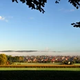 Hilter_Foto_Helmut Schmidt.JPG Blick auf ein Dorf unter blauem Himmel, umgeben von Feldern und herbstlich gefärbten Bäumen.