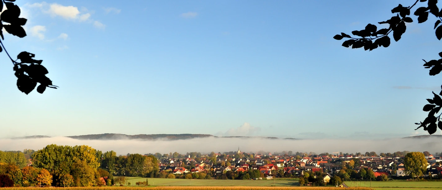 Hilter_Foto_Helmut Schmidt.JPG Blick auf ein Dorf unter blauem Himmel, umgeben von Feldern und herbstlich gefärbten Bäumen.