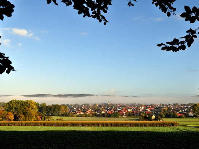 Hilter_Foto_Helmut Schmidt.JPG Blick auf ein Dorf unter blauem Himmel, umgeben von Feldern und herbstlich gefärbten Bäumen.