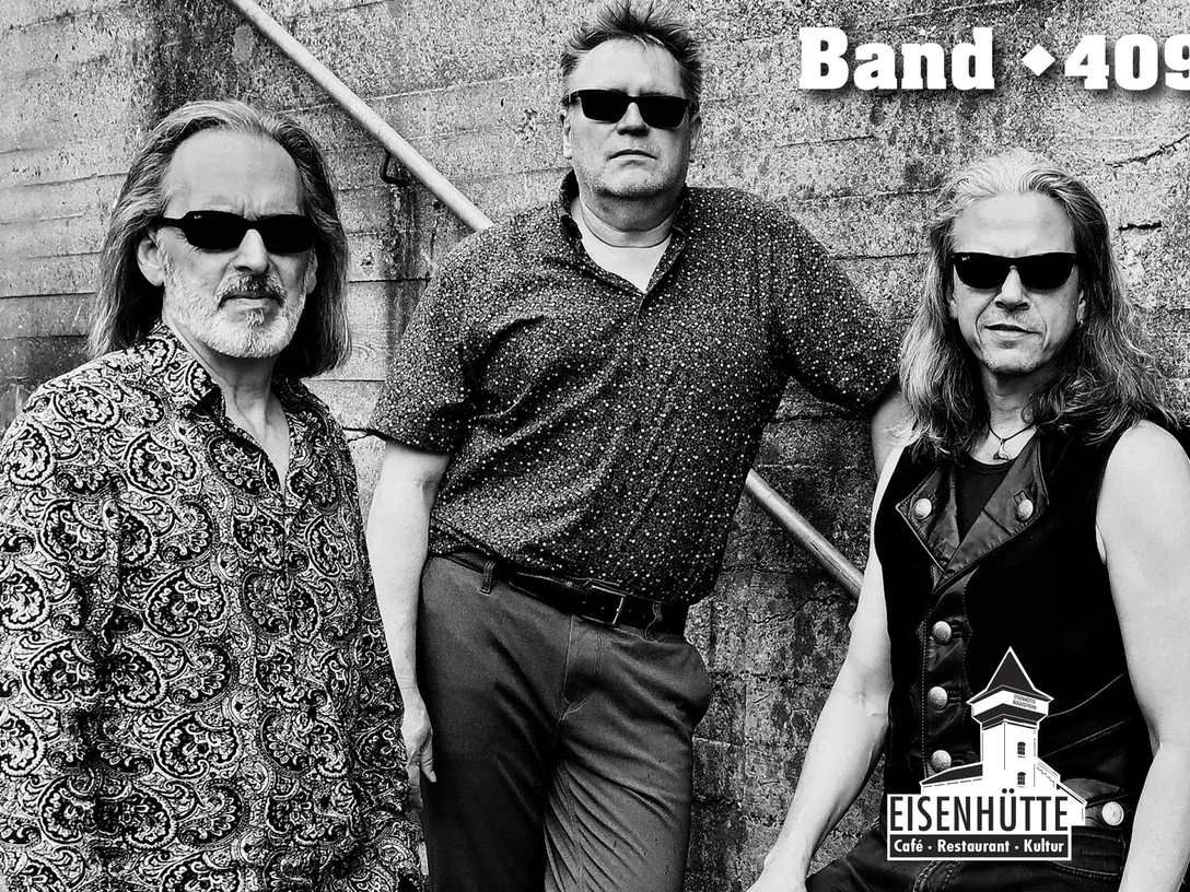 Band 409.jpg Drei Männer mit Sonnenbrillen posieren vor Betonwand, Schriftzug Band 409 und Logo Eisenhütte.Three men with sunglasses pose in front of a concrete wall with the lettering Band 409 and the Eisenhütte logo.Tre mænd med solbriller poserer foran en betonvæg med bogstaverne Band 409 og Eisenhütte-logoet.Drie mannen met zonnebrillen poseren voor een betonnen muur met het opschrift Band 409 en het logo van Eisenhütte.