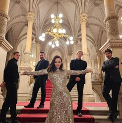 Sharon Brauner und Goy Boys Fünf elegant gekleidete Personen posieren auf roter Treppe in prunkvollem Saal.