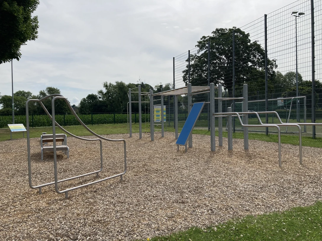 Eine Calisthenics-Anlage im Freien mit verschiedenen Trainingsgeräten auf einem holzgeschnitztem Boden.