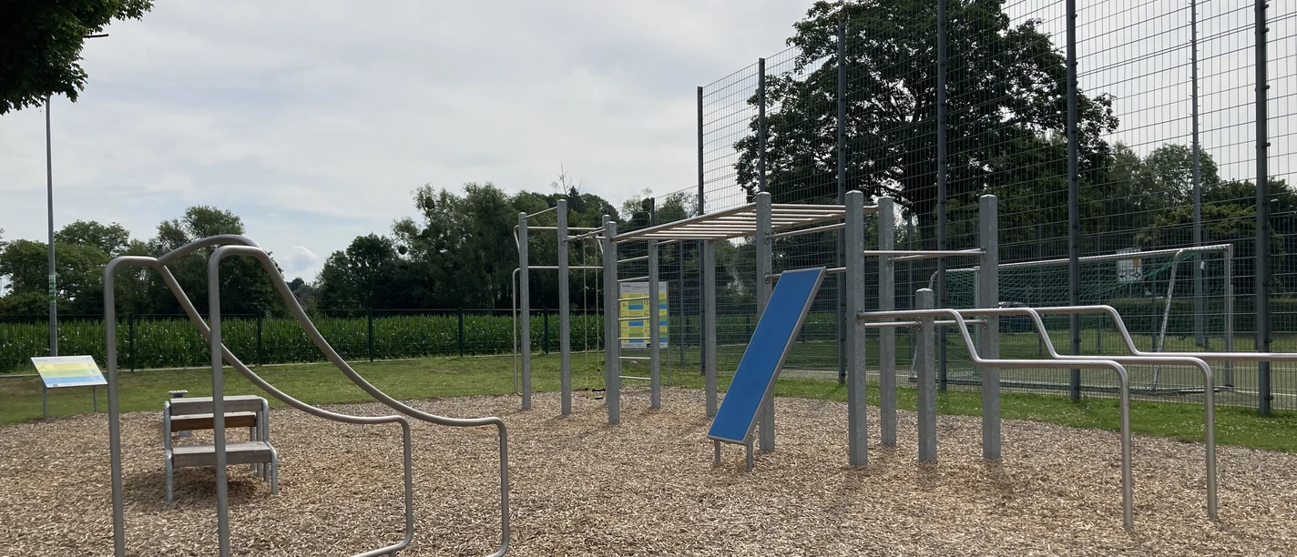 Eine Calisthenics-Anlage im Freien mit verschiedenen Trainingsgeräten auf einem holzgeschnitztem Boden.