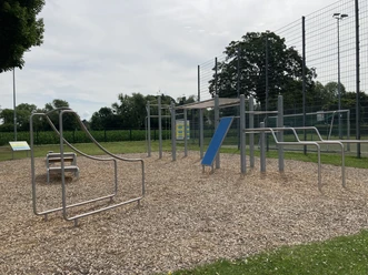 Borchen_Calisthenics-Anlage_05 ©Kreis Paderborn.jpeg Eine Calisthenics-Anlage im Freien mit verschiedenen Trainingsgeräten auf einem holzgeschnitztem Boden.