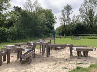Wasserspielplatz mit Holzrinnen und Sand, umgeben von Bäumen und Wiesen im Kreis Paderborn.