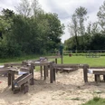 Wasserspielplatz mit Holzrinnen und Sand, umgeben von Bäumen und Wiesen im Kreis Paderborn.