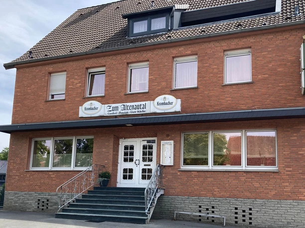 Borchen-Etteln_Gasthof-zu,-Altenautal_01 ©Kreis Paderborn.jpeg Gasthof im roten Backsteinbau mit überdachter Treppe und weißen Türen, umgeben von Bäumen.