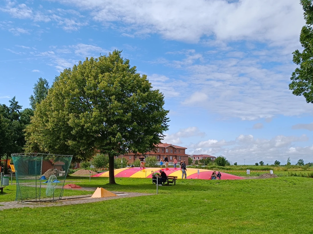 Großes Hüpfkissen Kinder toben auf einem großen rot-gelben Hüpfkissen auf einer weitläufigen grünen Spielwiese.