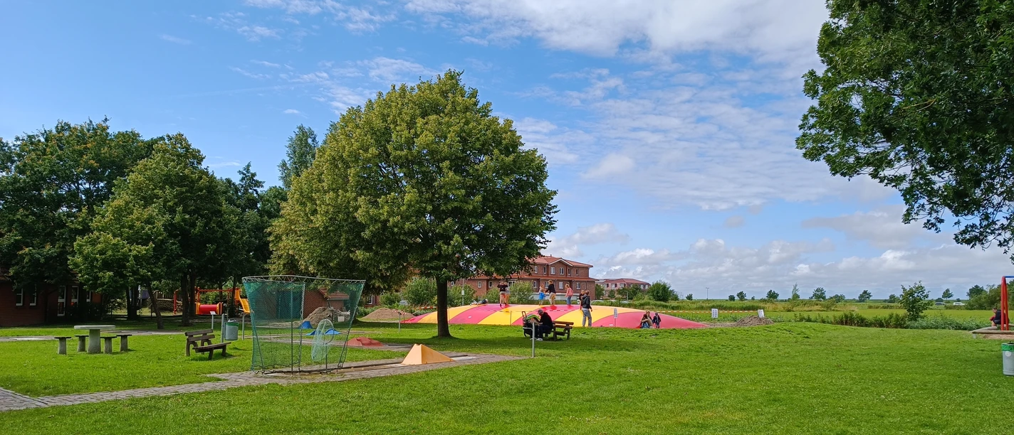 Großes Hüpfkissen Kinder toben auf einem großen rot-gelben Hüpfkissen auf einer weitläufigen grünen Spielwiese.
