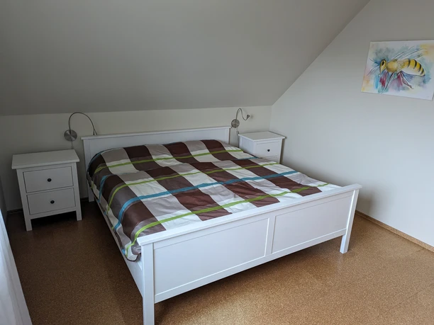 FW_Kurmann_Spelle2©A.Kurmann.jpg Helles Schlafzimmer mit Doppelbett, kariertem Bettbezug, zwei weißen Nachttischen und Wandleuchten.