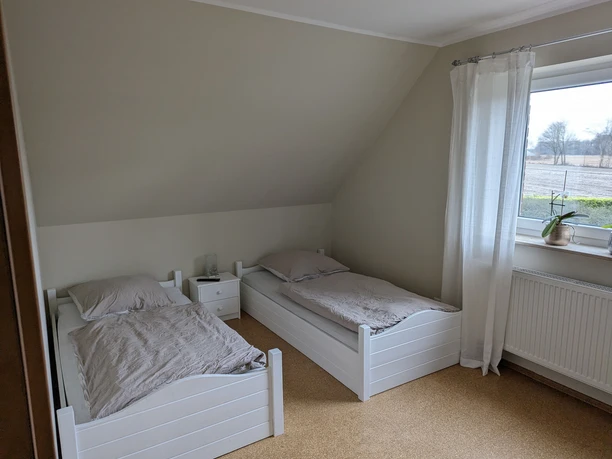FW_Kurmann_Spelle3©A.Kurmann.jpg Zweibettzimmer mit hellem Teppichboden, zwei weißen Betten, Nachttisch und Fenster mit Blick ins Freie.