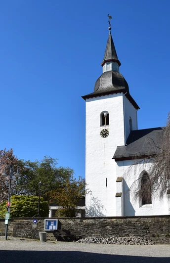 Bonte Kerke in Nümbrecht - Marienberghausen <p>Katholische Kirche mit weißer Fassade und Turm, umgeben von Fachwerkhäusern unter blauem Himmel.</p>