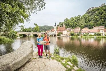 Kallmünz am Naabufer Ein Pärchen steht mit einer Übersichtskarte am Ufer der Naab, im Hintergrund ist der bekannte Künstlerort Kallmünz zu sehen