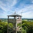 Borgholzhausen-Luisenturm-Teutoburger-Wald-Tourismus-D-Ketz-056.jpg Holzturm in grüner Landschaft mit Ausblick, zwei Personen geniessen die Aussicht unter blauem Himmel.
