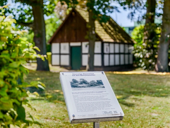 _BBB7326.jpeg Fachwerk-Gebäude im Grünen hinter einer Infotafel, umgeben von Bäumen und Schatten.