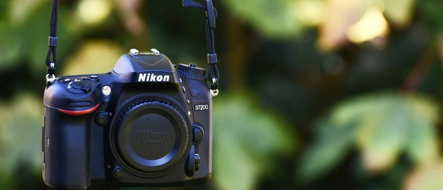 Fotografiekurs Eine Nikon D7200 Kamera hängt vor unscharfem, grünen Hintergrund.