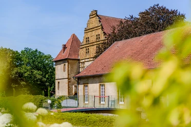Historische Burg mit rotem Ziegeldach umgeben von üppigem Grün, prunkvoller Renaissance-Giebel.