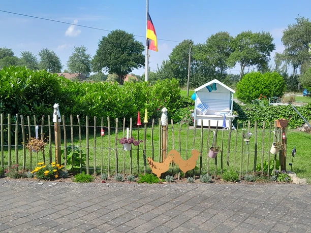 Ein gepflegter Garten mit schattigem Strandkorb, Flagge im Hintergrund und Dekoration entlang des Zauns.