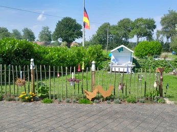 Garten.jpg Ein gepflegter Garten mit schattigem Strandkorb, Flagge im Hintergrund und Dekoration entlang des Zauns.
