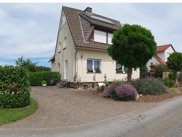 Hausansicht-1.jpg Ein Einfamilienhaus mit Satteldach, umgeben von gepflegtem Garten und gepflasterter Einfahrt.