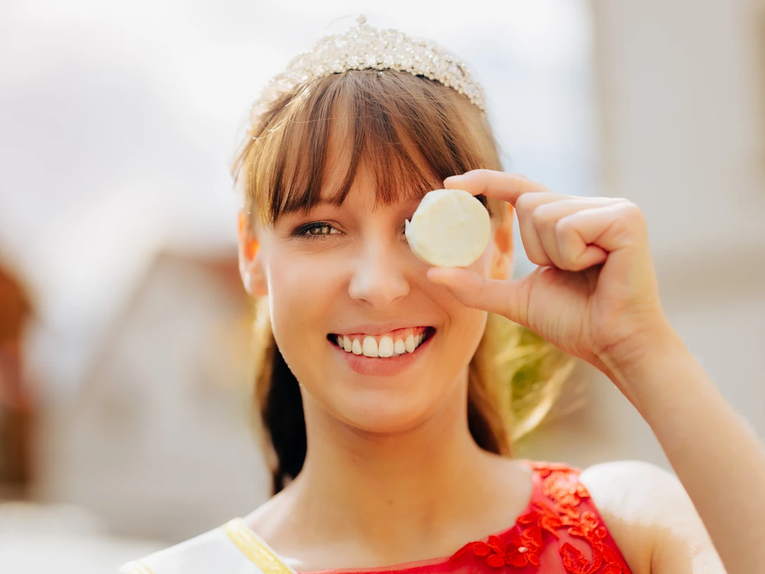 Käsekönigin Lena Schnelle mit dem Nieheimer Käse Lena Schnelle, die Käsekönigin, lächelt und hält stolz ein Stück des Nieheimer Käses vor ihr Auge.