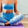 Sport Frauen_ Pixabay Person in blauem Sportoutfit sitzt im Schneidersitz auf einer lilafarbenen Yoga-Matte.