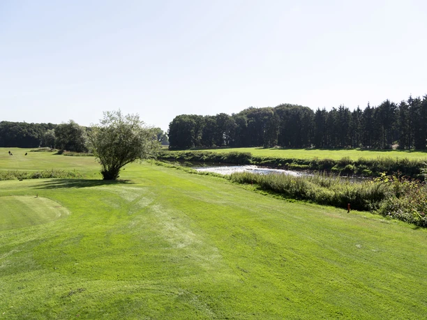 Golfclub Emstal © Emsland Tourismus GmbH (2).JPG Weitläufige Golflandschaft mit gepflegtem Rasen, vereinzelten Bäumen und Flusslauf im Sonnenlicht.