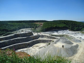 Steinbruch mit mehreren terrassierten Ebenen und Wald im Hintergrund, unter blauem Himmel gelegen.
