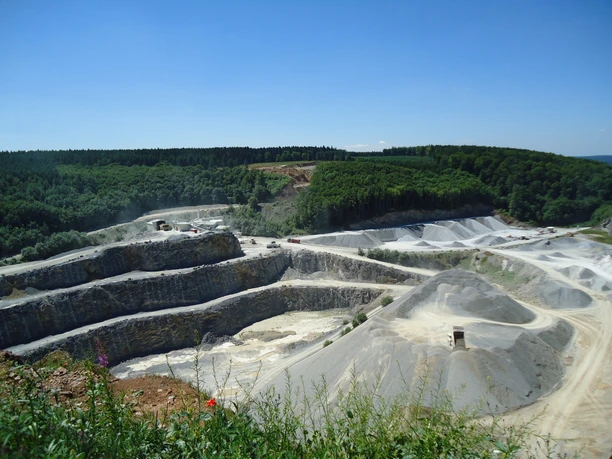 Bad-Wuennenberg_Steinbruch_01_©Bad-Wuennenberg-Touristik-GmbH.JPG Steinbruch mit mehreren terrassierten Ebenen und Wald im Hintergrund, unter blauem Himmel gelegen.