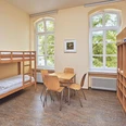 JGH-Petershagen-060_bearbeitet.jpg Ein heller Raum mit Etagenbetten, einem Tisch, Stühlen und großen Fenstern mit Blick ins Grüne.