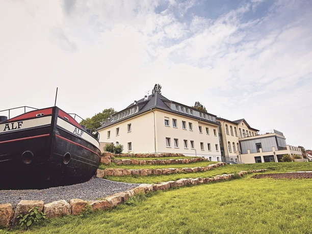 JGH-Petershagen-120_bearbeitet.jpg Das Bild zeigt ein modernes Gebäude, flankiert von einem Schiffsbug und von gepflegten Rasenflächen umgeben.