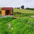 Talblick Bärenquelle Holzhütte mit Terrasse und Tischgarnitur, umgeben von Blumenwiese und kleinem Bachlauf.