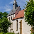 Eine historische Kirche mit spitzem Turm und rotem Ziegeldach, umgeben von grünen Bäumen.