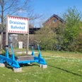 Eine blaue Draisine steht auf einem Rasenstück vor einem Schild mit der Aufschrift „Draisinen-Bahnhof“.